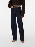 Model in donkerblauwe jeans met wijde pijpen en gele stiksels, gedragen met een bruine kabeltrui.