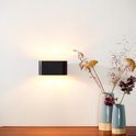 Zwarte XERA wandlamp, ovale vorm, met gouden binnenkant, boven een houten meubel met vazen.