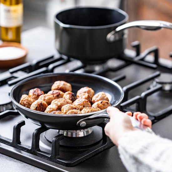 Poêle avec des boulettes de viande sur une cuisinière à gaz, la main d'une personne la tenant.
