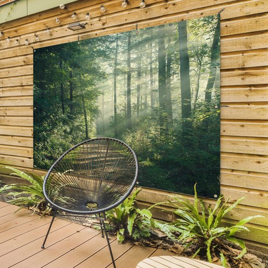 Un sentier forestier avec des rayons de soleil, accroché à un mur en bois avec une chaise devant.
