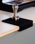 Zwarte tampermat met een zilveren tamper erop, geplaatst op een wit werkblad.
