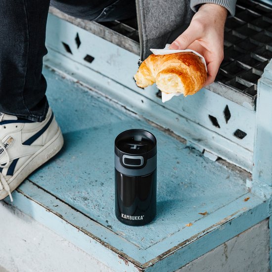 Thermos Kambukka noir à côté d'un croissant sur un petit escalier.