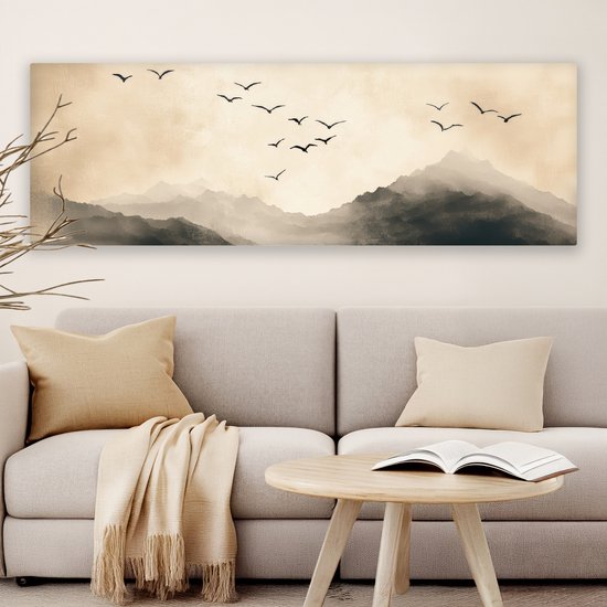 Une toile panoramique avec des montagnes et des oiseaux en vol, dans des tons sépia, au-dessus d'un canapé avec des coussins et un plaid.