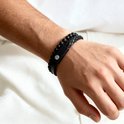 Zwarte gevlochten lederen armband met kralen van zwarte lavasteen en mat zwart, gedragen om een mannenpols.