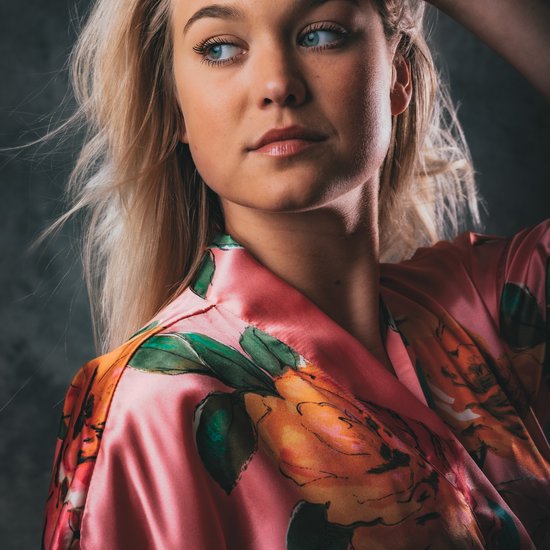 Close-up van model in koraalrode satijnen kimono met opvallende bloemenprint.