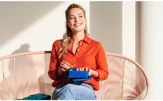 Femme souriante en chemise orange tenant une boîte à pain bleue.