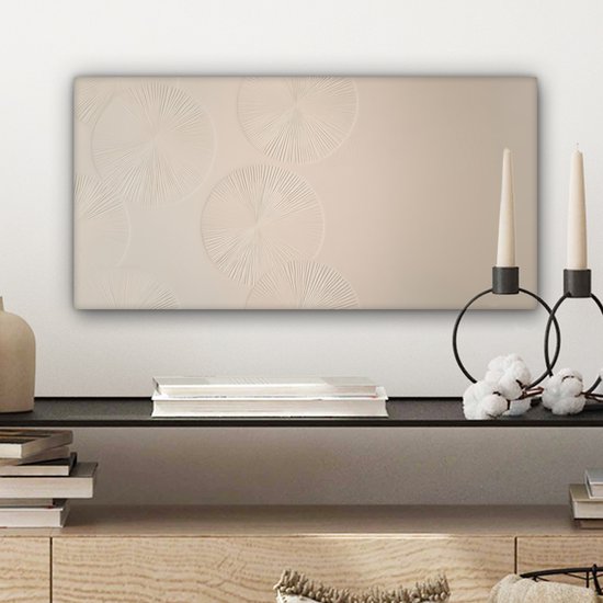 Beige canvas met cirkelvormige patronen, hangend boven een zwarte plank met boeken en decoraties.