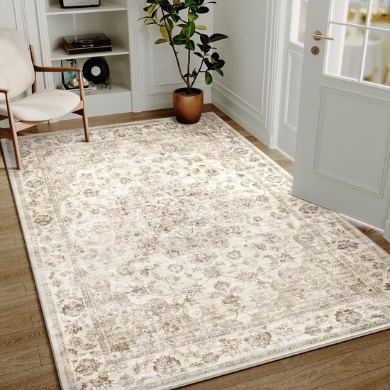 Tapis beige au motif floral classique et délavé, posé sur un parquet à côté d'une chaise.