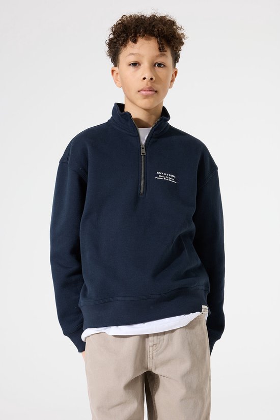 Jongen in donkerblauwe sweater met rits en beige broek, van voren.