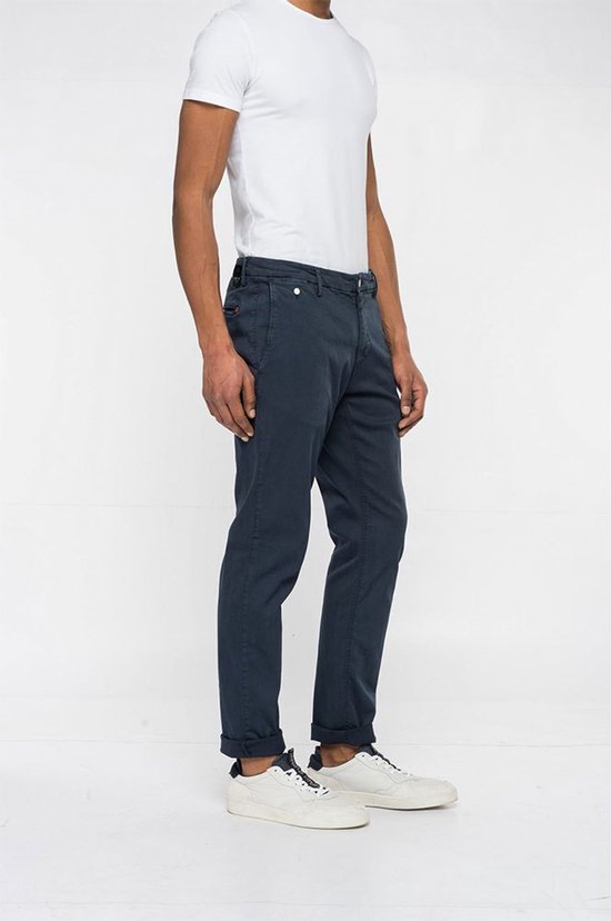 Man met donkerblauwe chino broek, omgeslagen broekspijpen en witte sneakers, zijaanzicht.