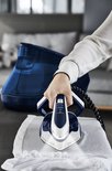 Hand met een witte blouse pakt het donkerblauwe en witte Tefal Pro Express Vision strijkijzer van een stuk wit textiel.