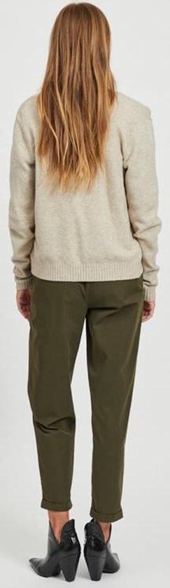 Model met blonde haren, rug naar camera, draagt een beige gebreid vest en olijfgroene broek.