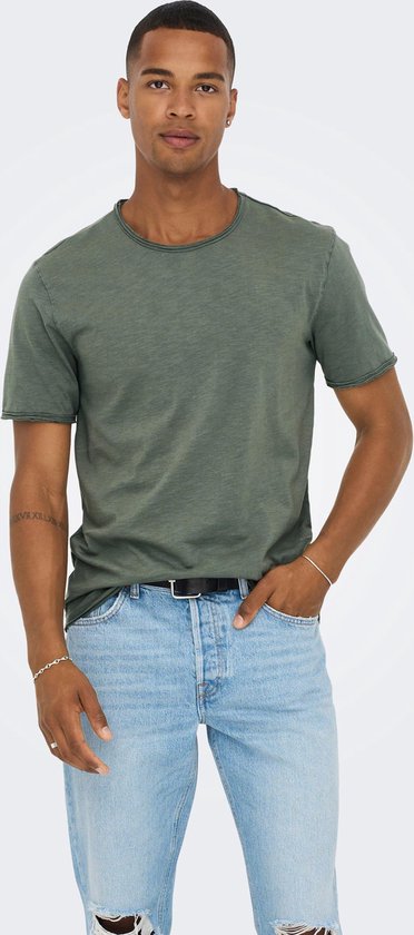 Man met olijfgroen t-shirt met korte mouwen en lichte gescheurde jeans.