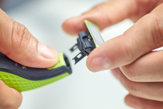 Gros plan de mains détachant une pièce jointe Philips OneBlade vert clair et argenté d'un appareil noir et vert.