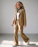 Model in bruine travelstof blazer en broek, wit t-shirt en zijden sjaaltje.