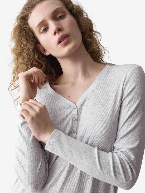 Close-up van een model met krullend haar, met een lichtgrijs, langgerokken nachthemd met knoopjes.
