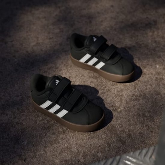 Twee zwarte adidas VL Court 3.0 schoenen met witte strepen en klittenband, bruine zolen.