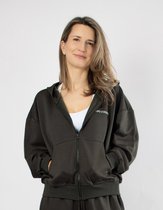 Model draagt een donkergroene, open rits hoodie met witte sportbeha en joggingbroek.