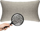 Een rechthoekig beige sierkussen met een teddy bouclé textuur. Een vergrootglas toont de fijne, gekrulde stofstructuur.