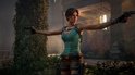Lara Croft in een groene top en bruine korte broek, houdt twee pistolen vast met uitgestrekte armen.