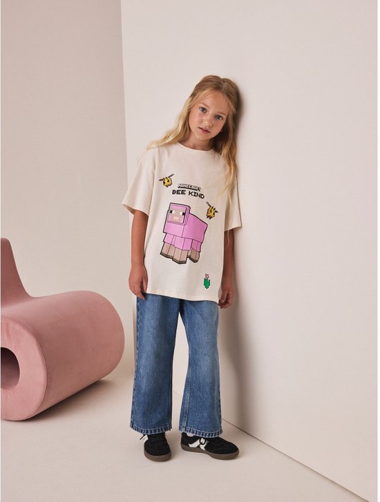 Crème oversized T-shirt met Minecraft print van een roze schaap en bijen. Gedragen door een meisje.