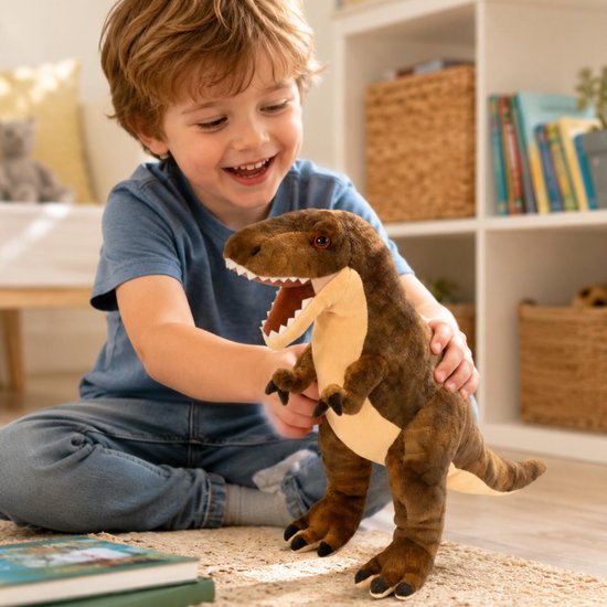 Jongen met een blauw shirt houdt een bruine pluche T-rex dinosaurus vast, zittend op de vloer.