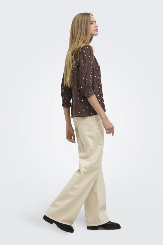 Model loopt in een bruine blouse met witte stippen en een off-white wijde broek.
