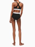 Zwarte Calvin Klein bralette met gekruiste bandjes op de rug en witte tailleband met logo, gedragen met bijpassende broek.