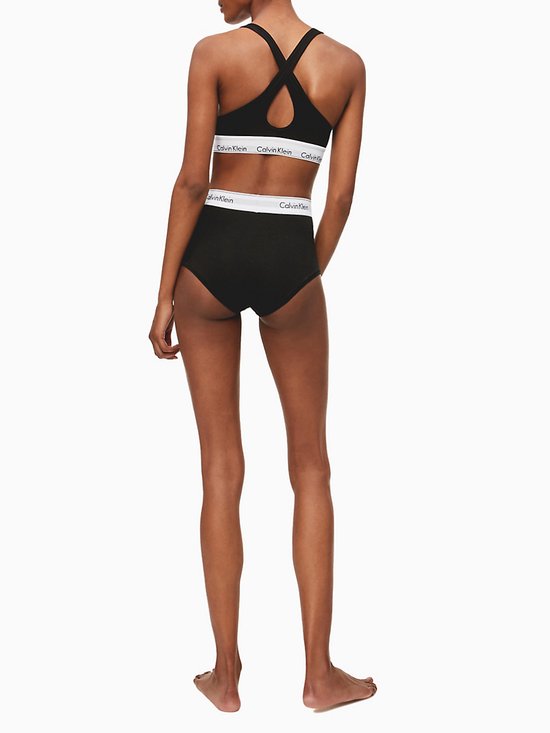 Zwarte Calvin Klein bralette met gekruiste bandjes op de rug en witte tailleband met logo, gedragen met bijpassende broek.