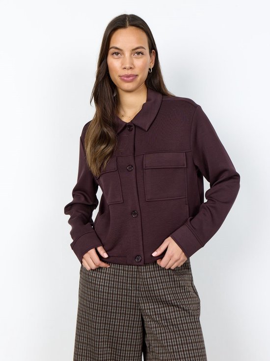 Model draagt donkerbruin vest met twee borstzakken, knoopsluiting en kraag, gecombineerd met geruite broek.