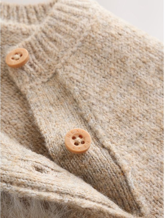 Close-up van de houten knopen en de gebreide stof van een beige baby trui.