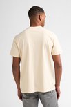 Man staat met de rug naar de camera, draagt een crème T-shirt met korte mouwen en grijze jeans.