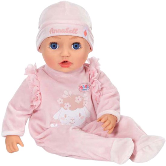 Zittende Annabell babypop in roze velours pakje met schaapprint. Draagt een roze mutsje met "Annabell" erop.