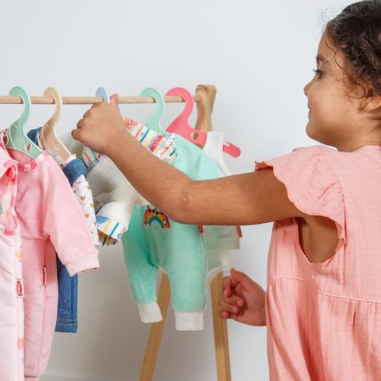 Meisje pakt een turquoise poppen romper met regenboog op de kleerhanger.
