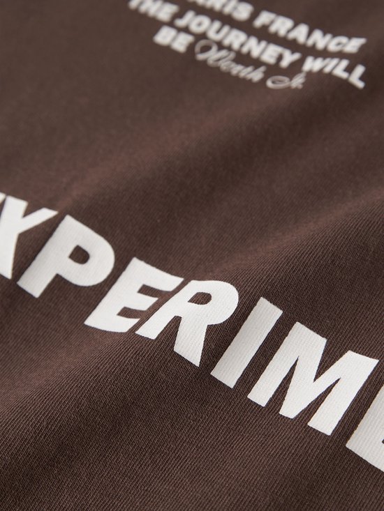 Detailopname van de witte tekst 'EXPERIMENTAL' op een bruin t-shirt.