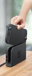 Hand die een grijze Nintendo Switch console in een zwart dockingstation plaatst.