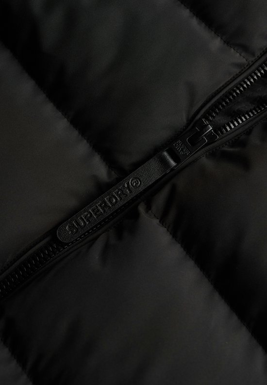 Close-up van de rits van een zwarte pufferjas met 'SUPERDRY' logo.