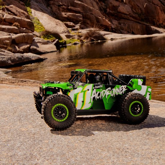 Groene en witte RC-auto "Acid Runner" met grote banden, zittend op een rots bij water.