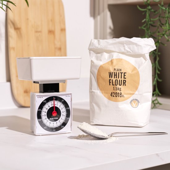 Witte keukenweegschaal met een ronde bak, naast een zak bloem met "PLAIN WHITE FLOUR 1.5kg" erop.