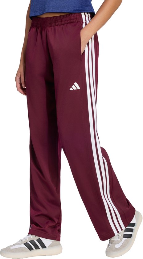 Bordeauxrode trainingsbroek met witte strepen aan de zijkant, gedragen door een model met de hand in de zak.