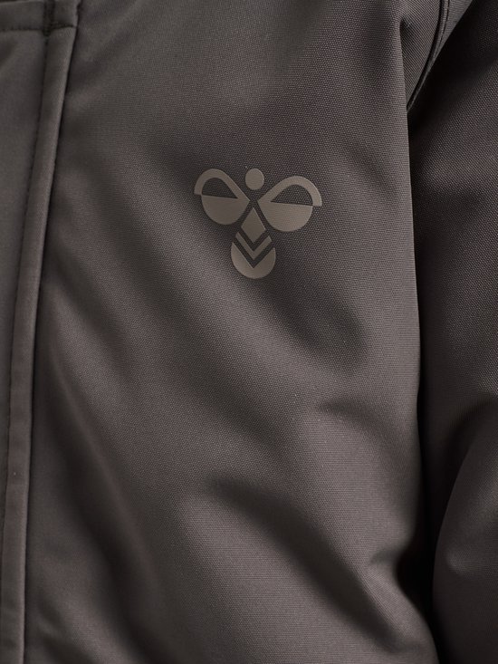 Detail van een donkergrijze jas met een geborduurd hummel-logo.
