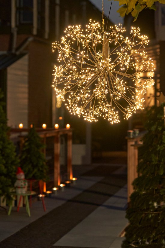 Une grande lampe de Noël sphérique avec des LED blanc chaud, suspendue à un fil à l'extérieur au-dessus d'un jardin.