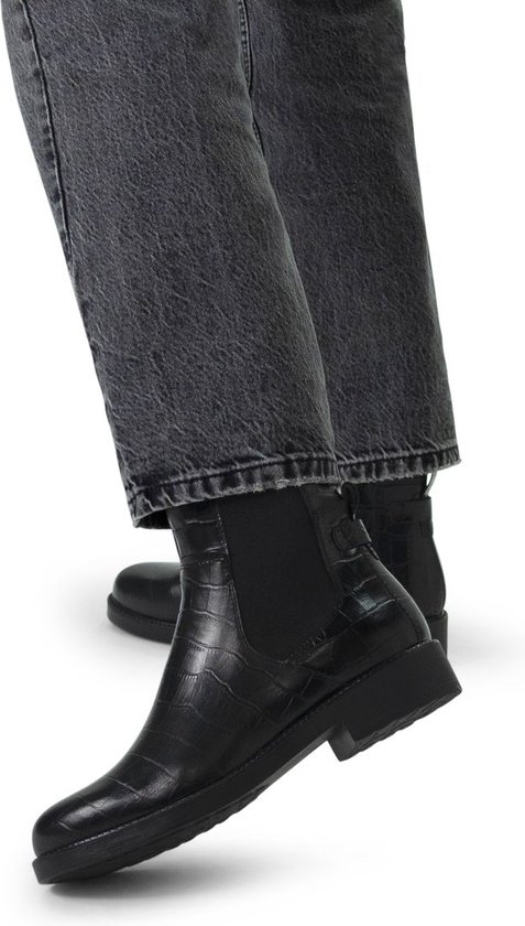 Model draagt zwarte leren chelsea boots met crocoprint en jeans.