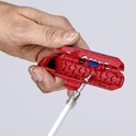 Een hand gebruikt een rode kabelstripper met blauwe accenten om een kabelscherm te verwijderen.