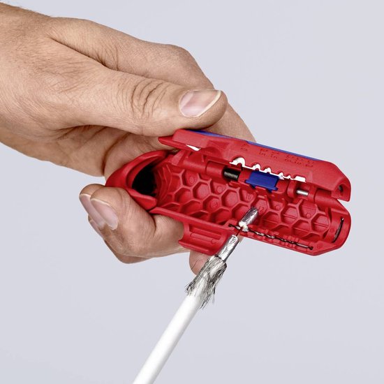 Een hand gebruikt een rode kabelstripper met blauwe accenten om een kabelscherm te verwijderen.