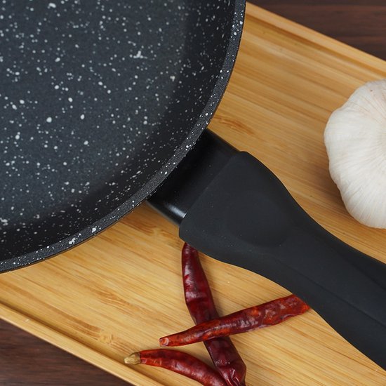 Detail van een zwarte koekenpan met granieten look, zwart handvat, met pepers en knoflook.