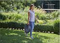 Vrouw met opgerolde grijze tuinslang in een weelderige groene tuin.