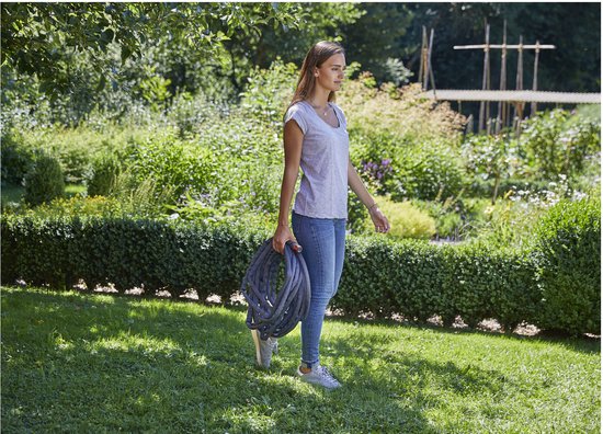 Vrouw met opgerolde grijze tuinslang in een weelderige groene tuin.