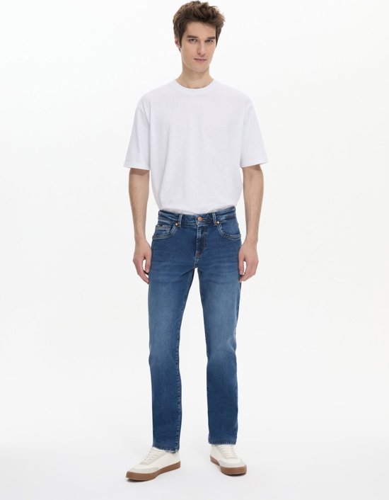 Man in een blauwe LTB jeans, staand met witte sneakers.
