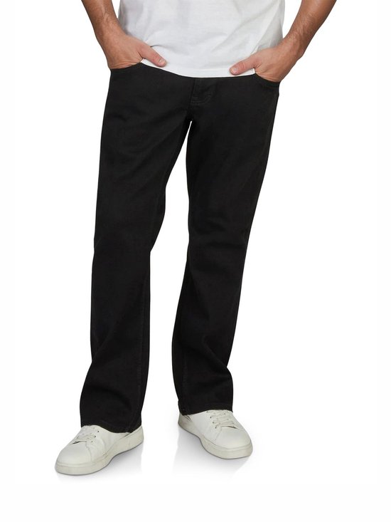 Vooraanzicht van een zwarte jeans met bootcut pasvorm. De man draagt de broek met witte sneakers en heeft zijn handen in de zakken.